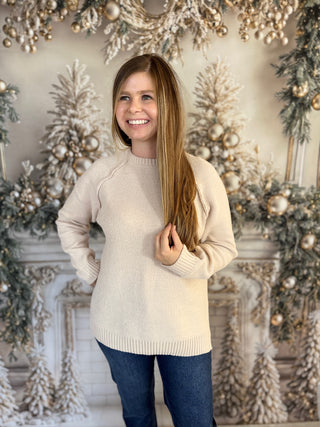 Woman in a beige sweater standing in front of a decorated Christmas background