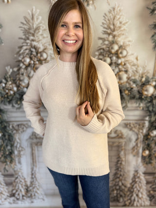 Young girl wearing a beige sweater in front of decorative Christmas trees.