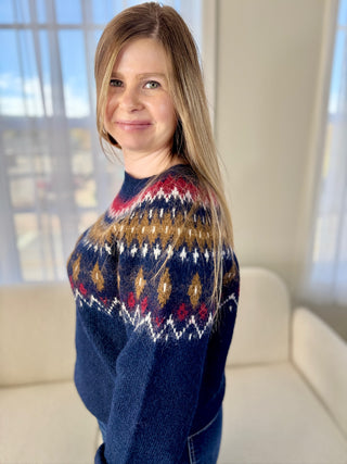 Woman wearing a blue sweater with a pattern, standing indoors.