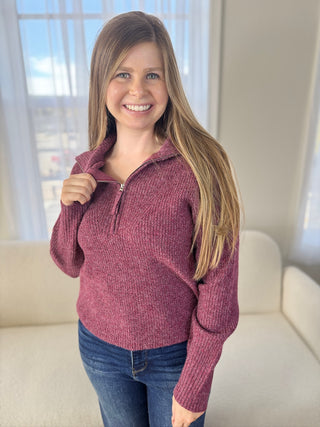 Woman wearing a maroon pullover with a zipper in a bright room.