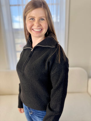 Woman wearing a dark sweater standing in a room with a window in the background