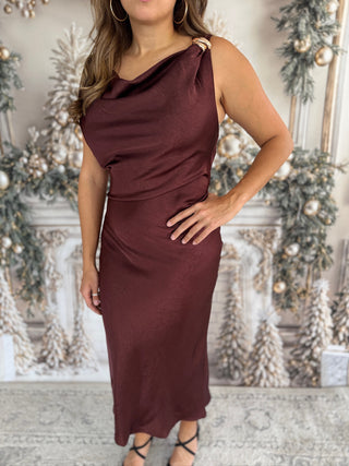 Woman wearing a burgundy one-shoulder dress in a decorated room.