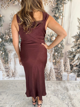 Woman wearing a burgundy dress in a festive indoor setting with Christmas decorations.