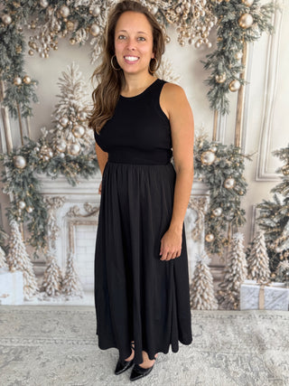 Woman in a black sleeveless dress standing in a decorated room with Christmas trees and ornaments.