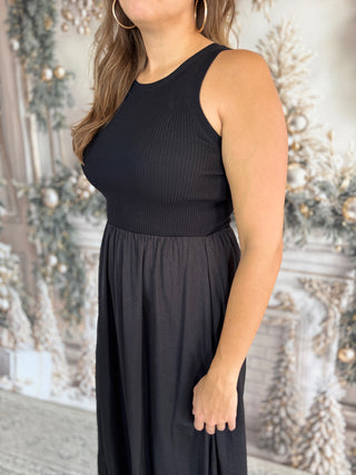 Woman wearing a black sleeveless top and long skirt against a decorative background