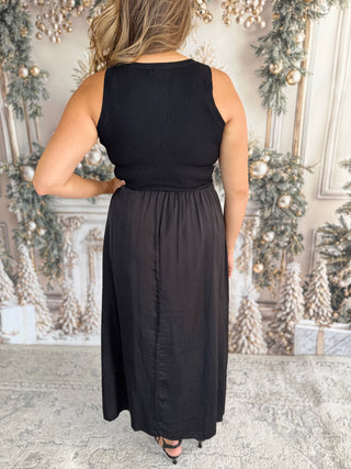 Woman wearing a black sleeveless top and long skirt in a decorated room.