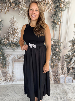 Woman in a black dress with a white bow standing in a decorated room.