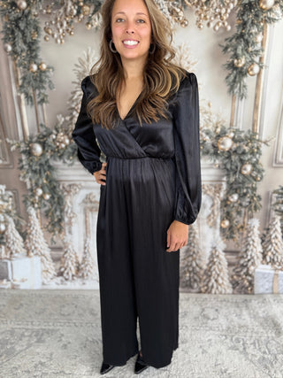Woman wearing a black jumpsuit in a decorated room with Christmas trees.