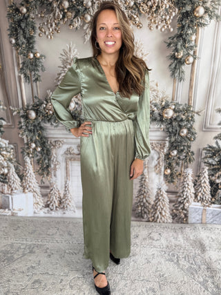 Woman in a green satin dress standing in front of a decorated Christmas wall.