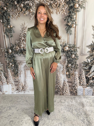 Woman in a green satin jumpsuit standing in front of a decorated Christmas background.