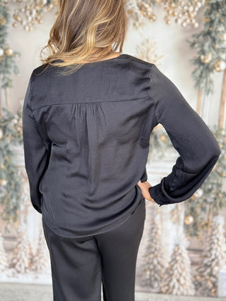 Person wearing a black long-sleeve top and pants against a decorative background