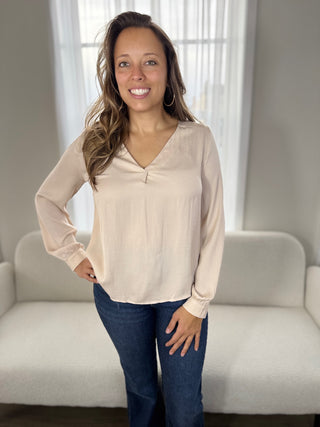 Woman wearing a beige blouse and blue jeans standing in a room with a neutral color scheme.