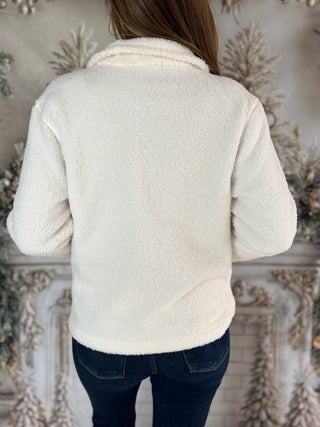 Person wearing a white sherpa jacket in front of a decorative wall.