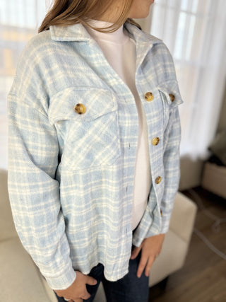 Person wearing a light blue plaid jacket with gold buttons indoors.