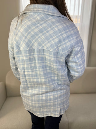Person wearing a blue and white plaid shirt sitting on a couch.