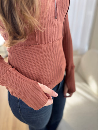 Person wearing a ribbed brown sweater with a zipper, standing indoors.