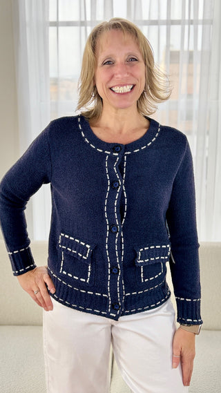 Woman wearing a navy blue cardigan with white stitching in a bright room.