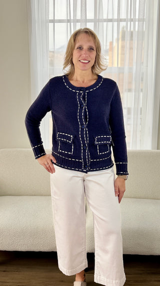 Woman wearing a navy blue sweater with white trim and white pants standing in a living room.