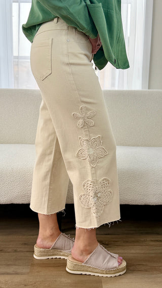 Person wearing beige pants with floral embroidery in a living room setting.