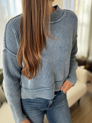Person wearing a blue and white patterned sweater and jeans indoors.