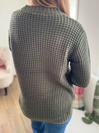 Person wearing a green knitted sweater in an indoor setting