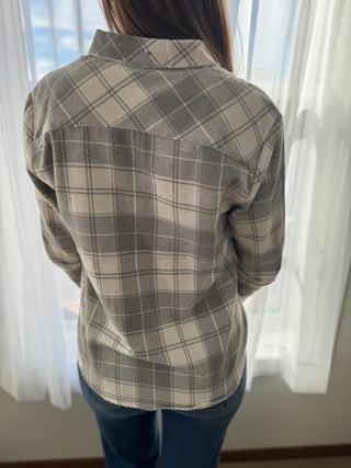 Person wearing a plaid shirt with a neutral color palette in front of sheer curtains.