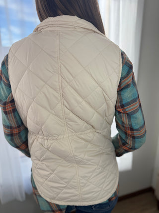 Person wearing a beige quilted vest over a plaid shirt with a neutral background