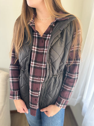 Person wearing a plaid shirt and gray quilted vest indoors