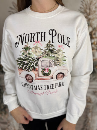 White sweatshirt with Christmas-themed design featuring a truck and trees, worn by a person.