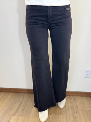 Person wearing dark blue flared jeans with a white shirt and white shoes on a plain background.