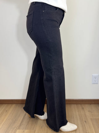 Person wearing black wide-leg jeans and white shoes on a plain background