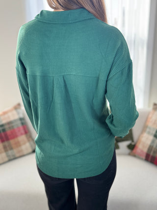 Person wearing a teal sweater in a room with light-colored walls and a couch.