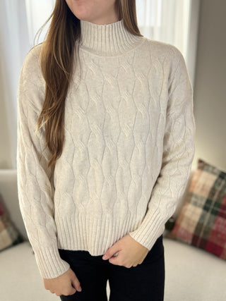 Person wearing a cream cable knit sweater in a neutral setting