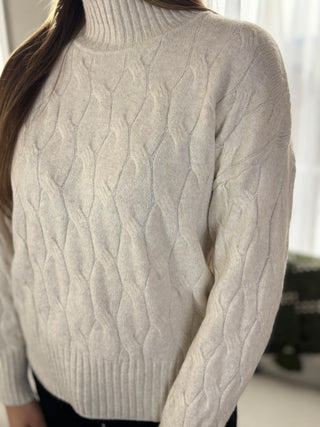 Close-up of a person wearing a cable knit sweater with a blurred background