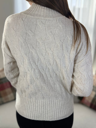 Person wearing a light gray cable knit sweater with blurred background