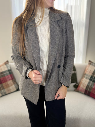 Person wearing a gray blazer over a white shirt in a living room setting.