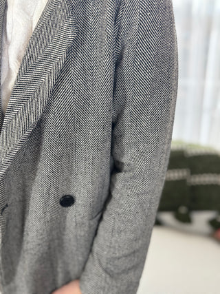 Gray herringbone patterned blazer with a single button on a blurred background
