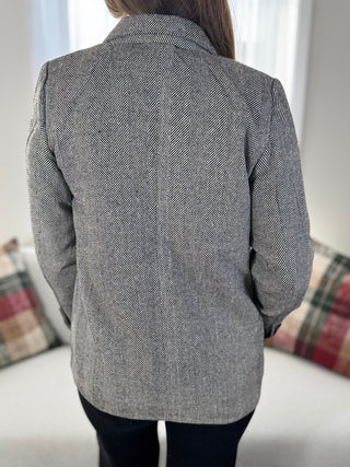 Person wearing a gray herringbone patterned coat in a room with plaid cushions.