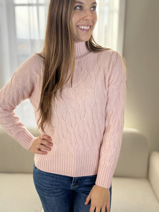 Woman wearing a pink cable knit sweater in a neutral setting