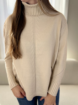 Person wearing a beige turtleneck sweater with a neutral background