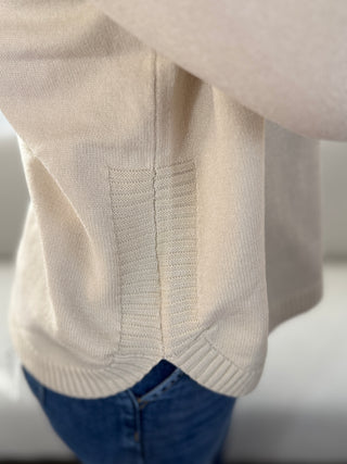 Close-up of a beige sweater with blue jeans in the background