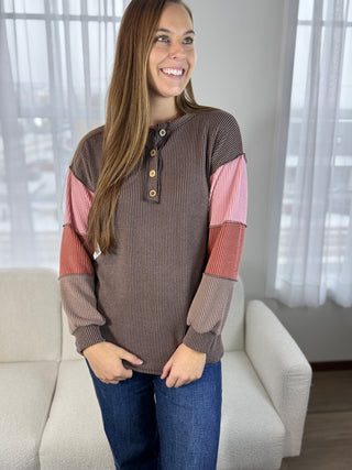 Woman wearing a colorful long-sleeve shirt standing in a room with a couch and window.