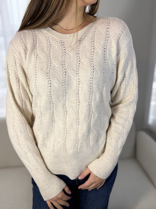 Person wearing a cream cable knit sweater in a neutral setting