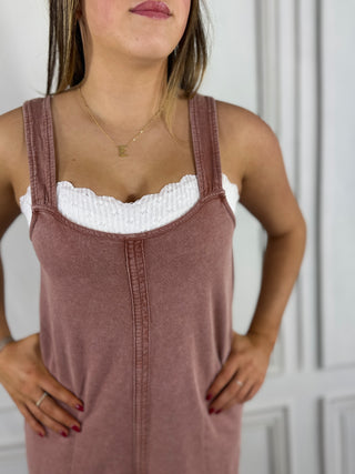 Woman wearing a brown dress with white lace top against a white wall.
