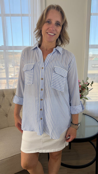 Woman wearing a blue and white striped shirt and white skirt indoors.