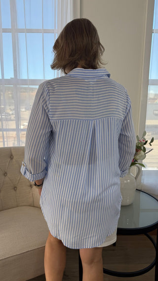 Person wearing a blue and white striped dress standing in a room with large windows.