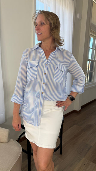 Woman wearing a blue and white striped shirt and white shorts indoors.