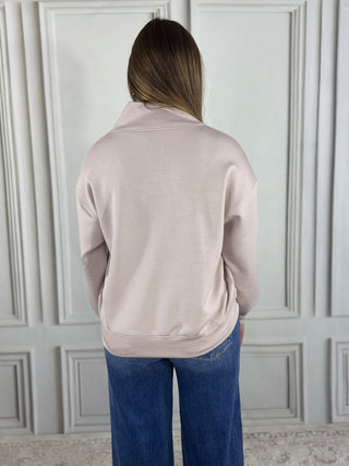 Person wearing a light gray jacket and blue jeans against a white paneled wall.