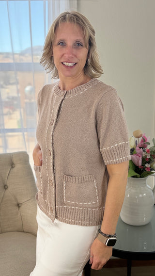 Woman wearing a brown short-sleeve cardigan with white trim in a living room.