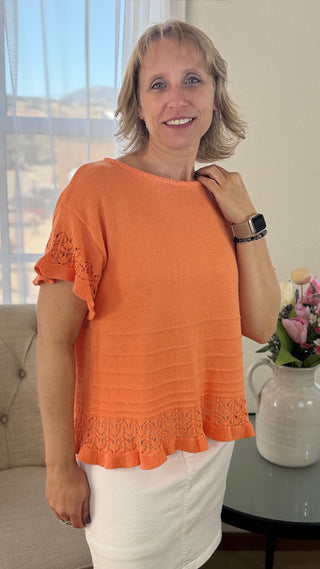 Woman wearing an orange top with lace sleeves in a home setting